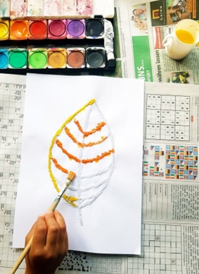 Childs hand painting a fall leaf with paint colors and a paintbrush