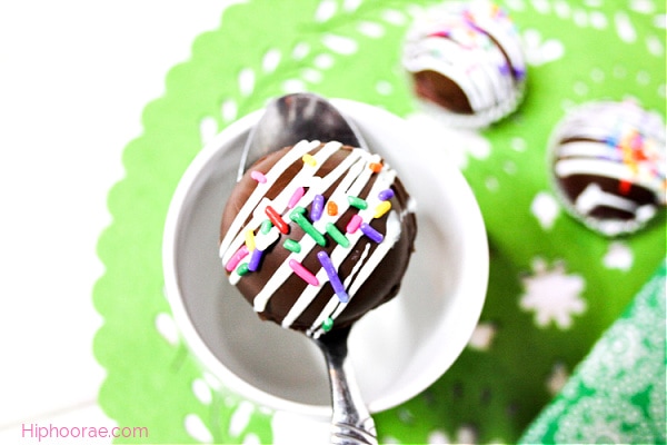 Hot Chocolate Bombs with sprinkles on a spoon above a mug
