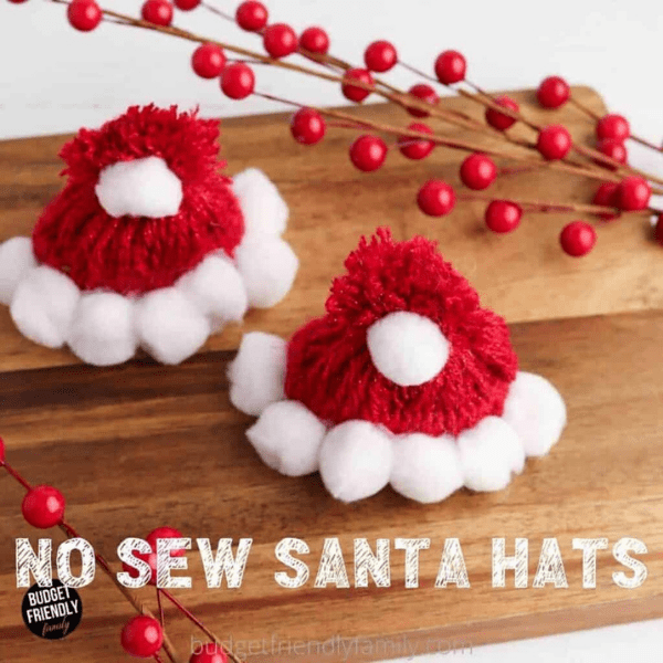 2 x Santa Hat Crafts made with yarn and white pom poms. on a wooden board