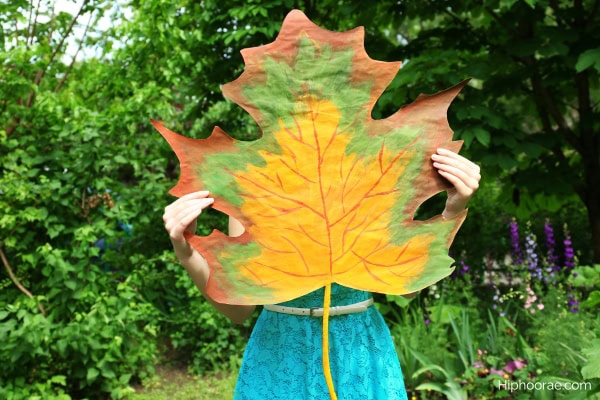 Woman holding up a huge maple leaf that covers half her body