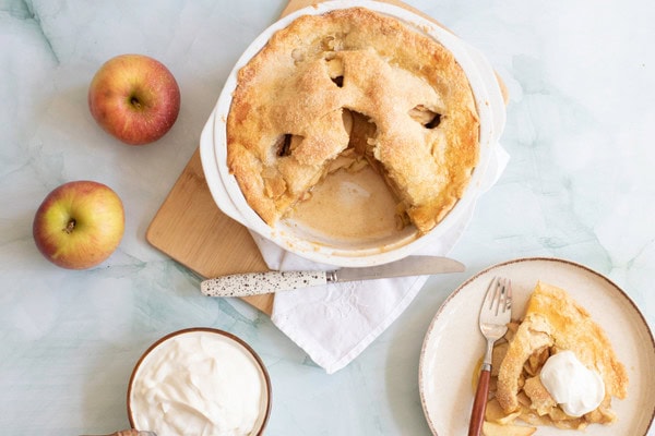 apple pie and a slice of pie on plate with 2 apples on the side