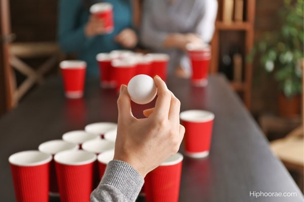 Someone about to throw a ping pong ball into plastic cups