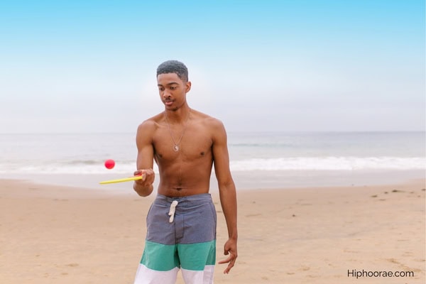 man bouncing a ping pong ball on a paddle in the beach