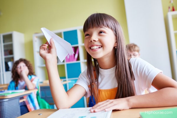 girl in classroom holding a paper airplane 