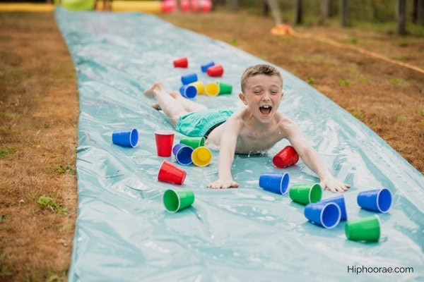 boy sliding on a tarp filled with plastic cups