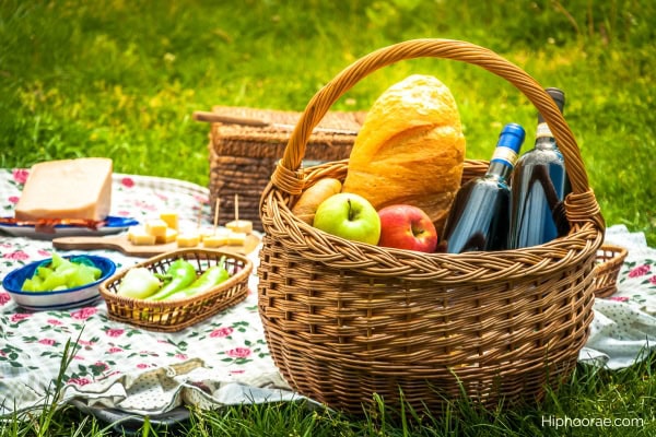 picnic setup with food and basket filled with apples, bread, wine