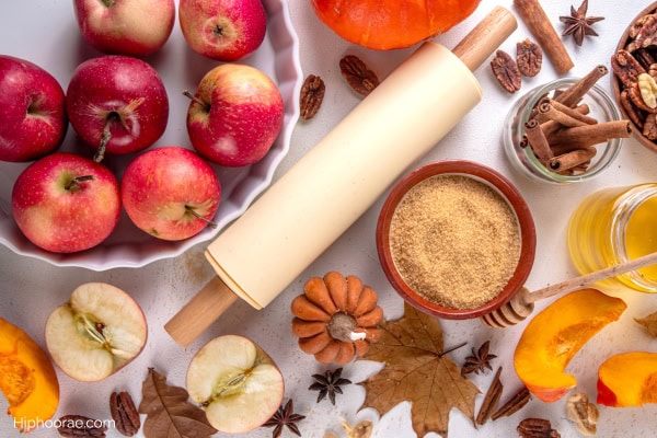 table filled with apples, pumpkins, cinnamon, and a rolling pin in the middle