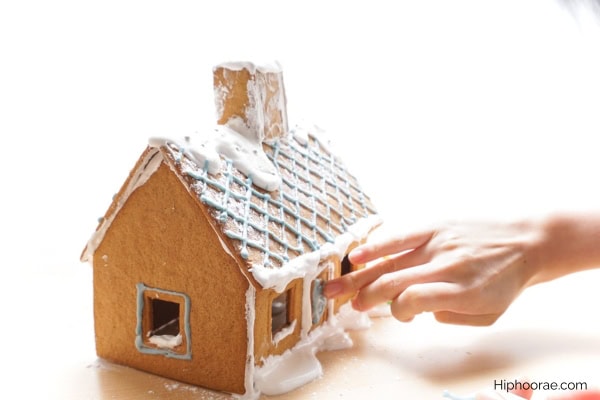 hands decorating a gingerbread house