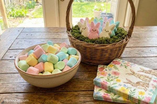Basket with bunny-shaped marshmallows, bowl full of pastel colored marshmallows, Easter-themed table napkins