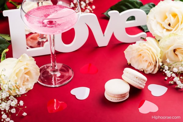 Valentine's day background of pink cocktail, white roses, white macarons, wooden word LOVE