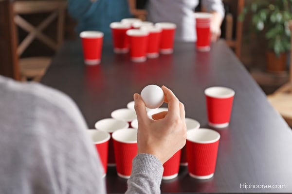 woman holding a ping pong ball to throw and try to shoot into a cup